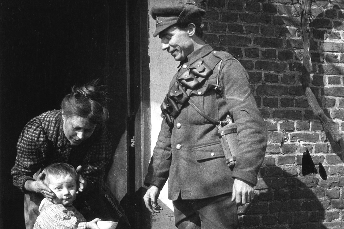 Black and white photograph of a soldier in First World War army uniform standing in his doorway with his wife and young child