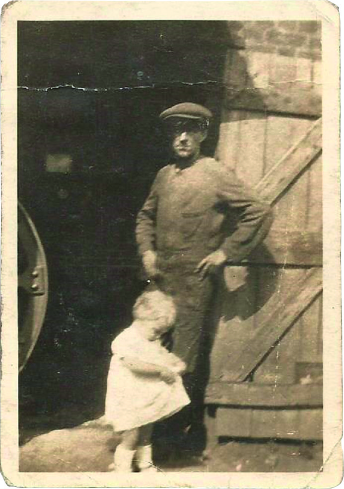 Black and white photograph of a man in a flat cap and a toddler in a white dress