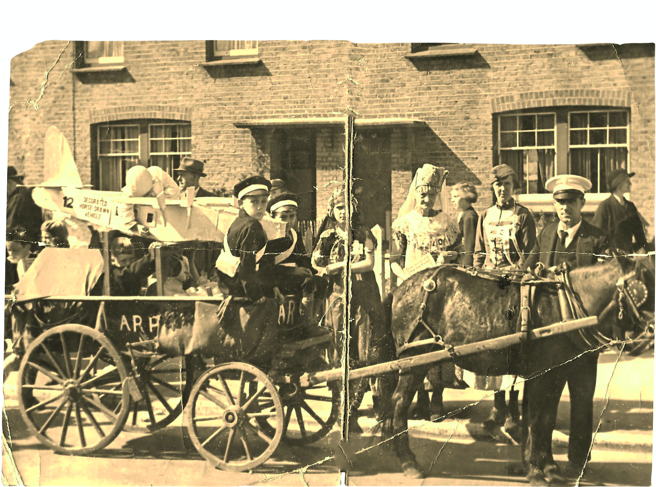 Black and white photograph of a group of children riding a pretend milk cart and horse while some adults stand around