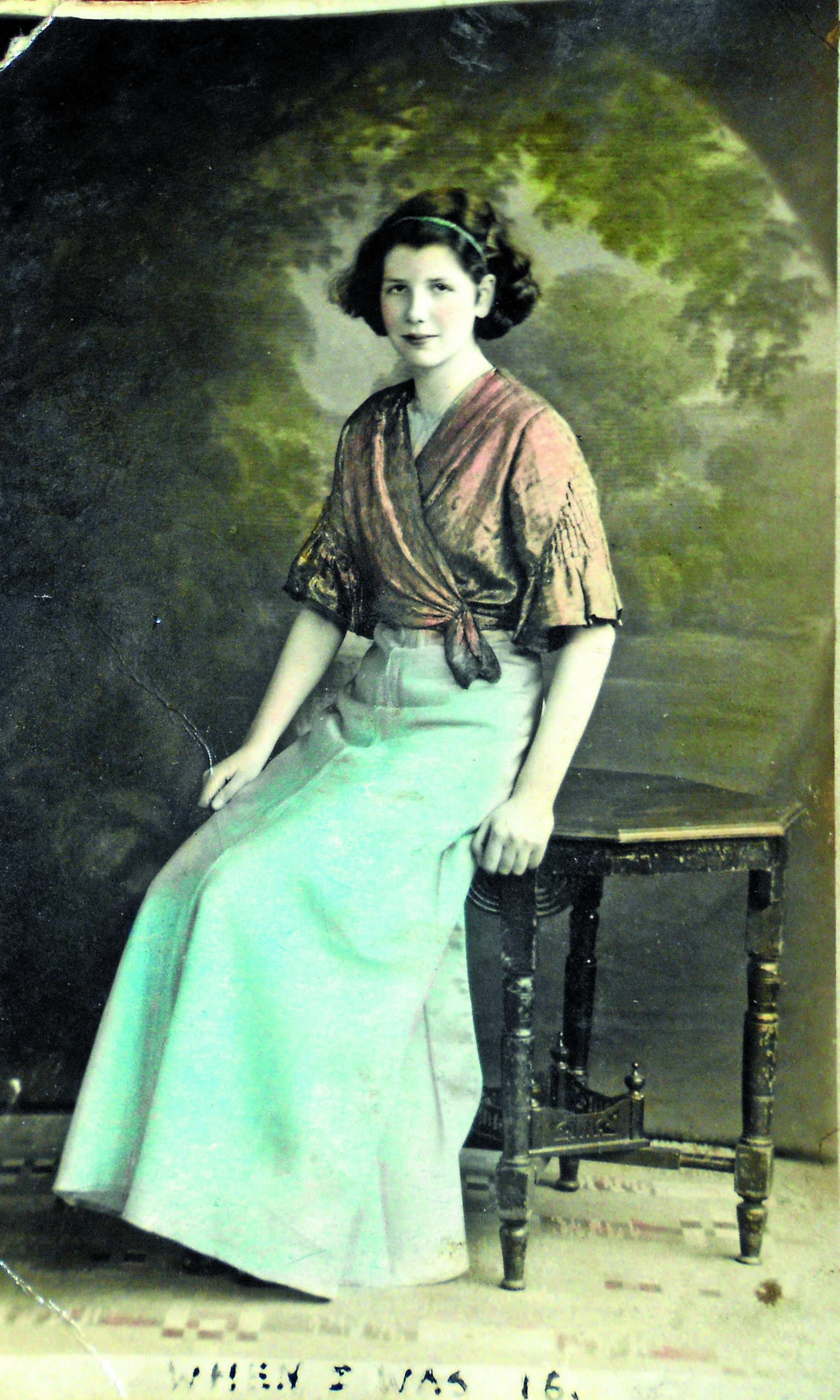 Colour-tinted photograph of a young woman with brown hair wearing an orange shawl and long blue skirt.