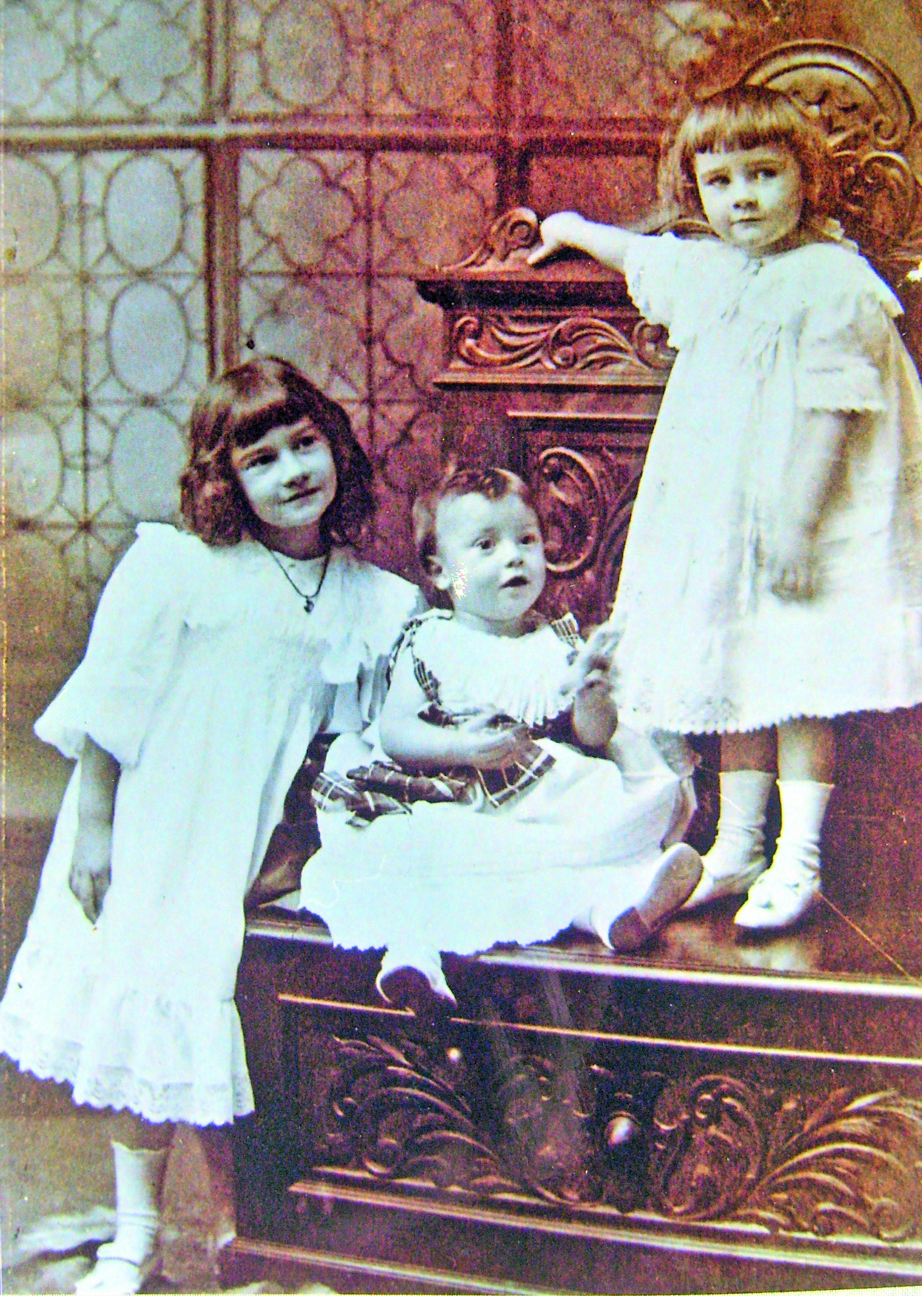 Black and white photograph of three children in old-fashioned white dresses