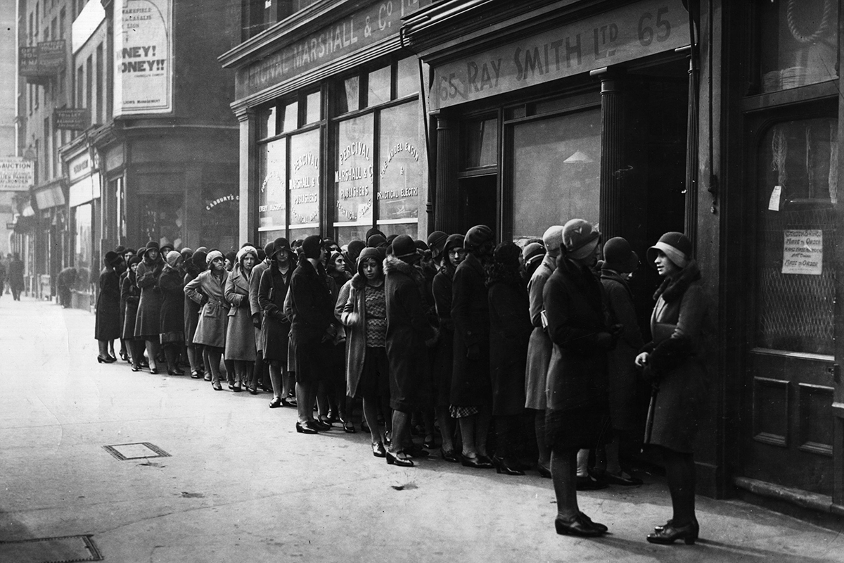 A black and white photograph of women in 1930s clothing queuing on a city street