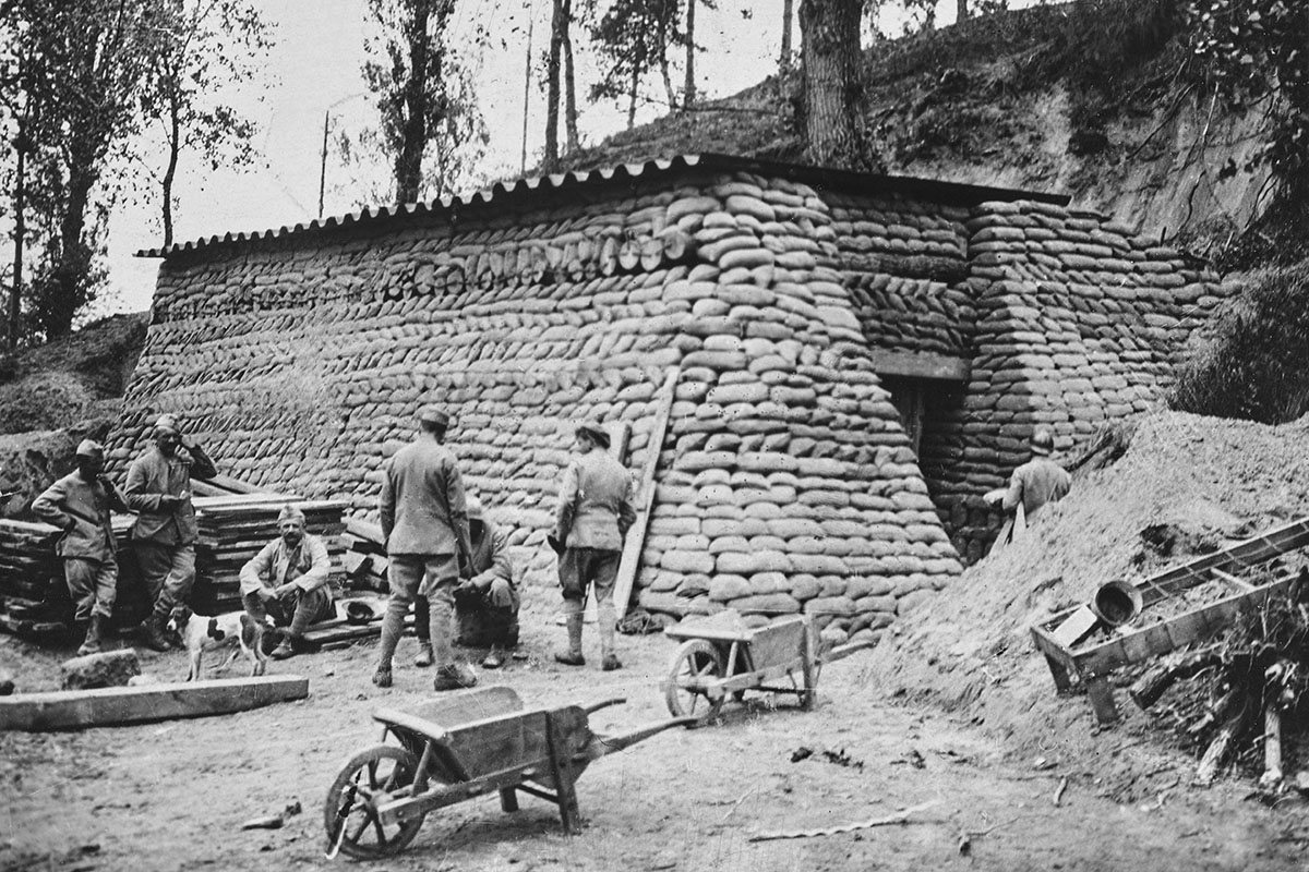 Black and white photograph showing First World War soldiers beside a bunker made out of sandbags, with a white dog with a brown patch