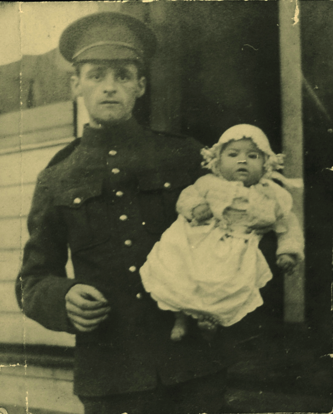 Black and white photograph of a young man in military uniform holding a baby in a white robe