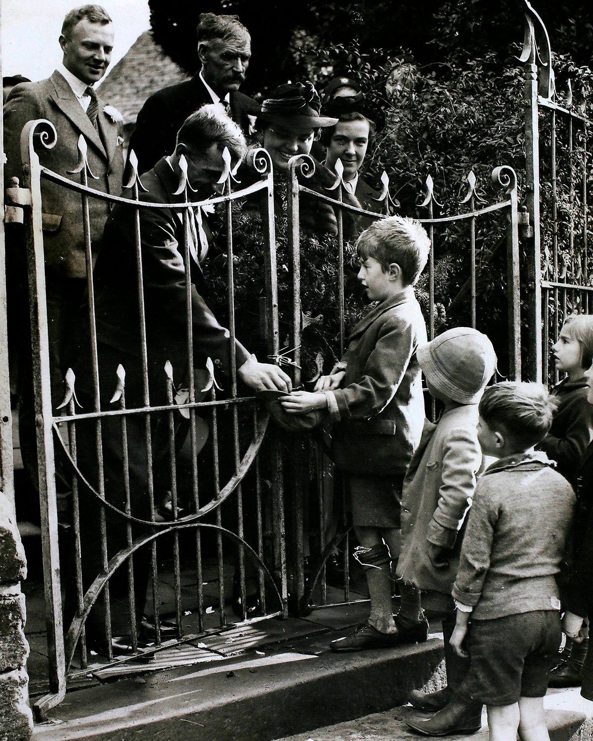 Black and white photograph of a man handing some small children money through a gate