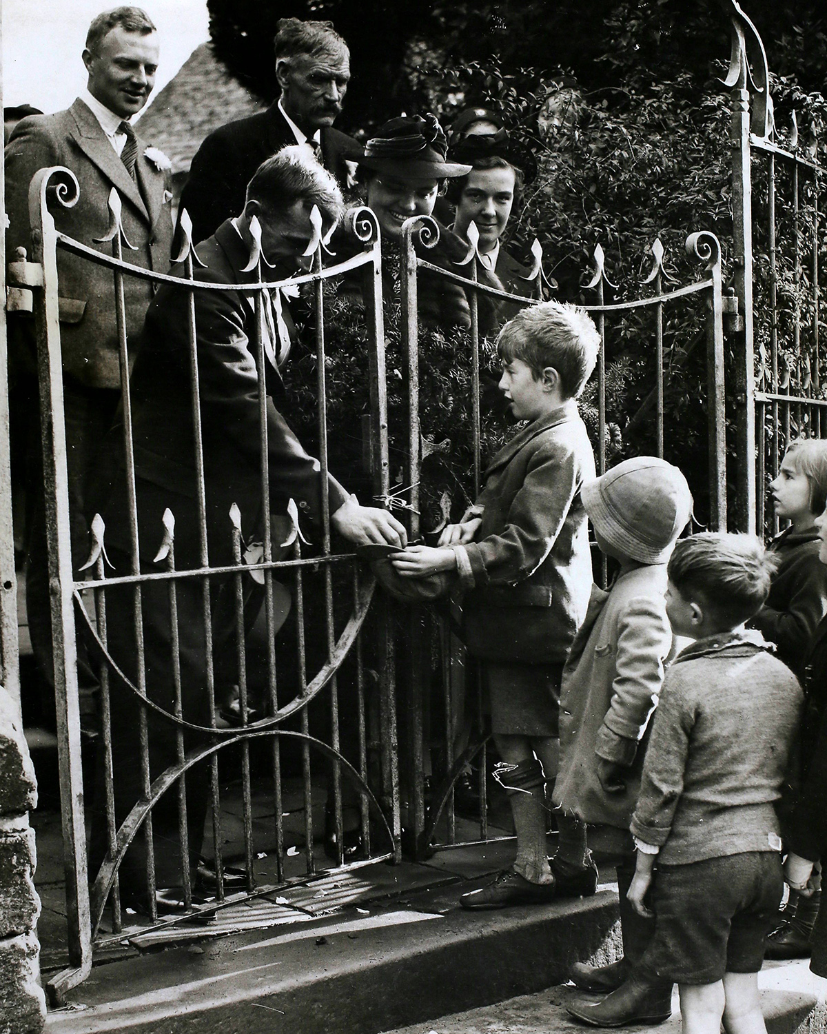 Black and white photograph of a man handing some small children money through a gate