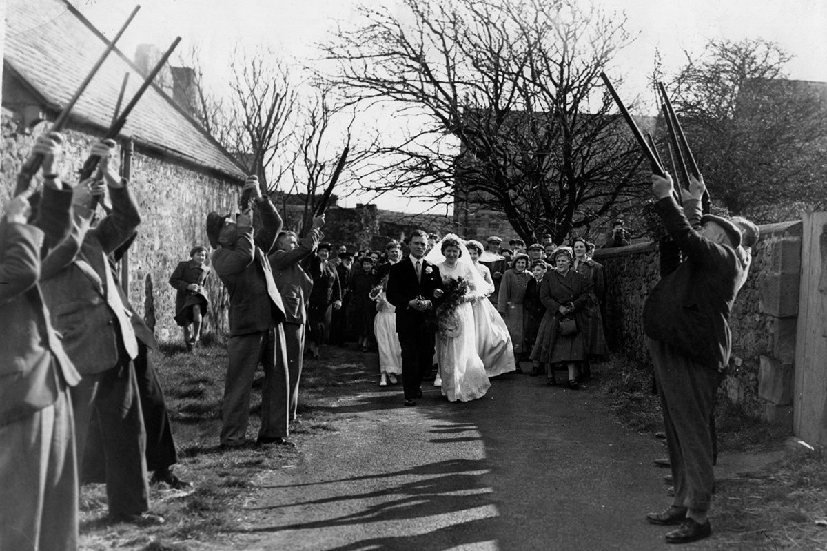 Black and white photograph of a bride and groom walking through a salute of guns