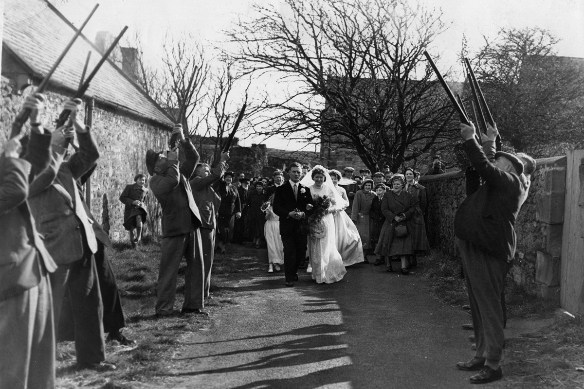 Black and white photograph of a bride and groom walking through a salute of guns
