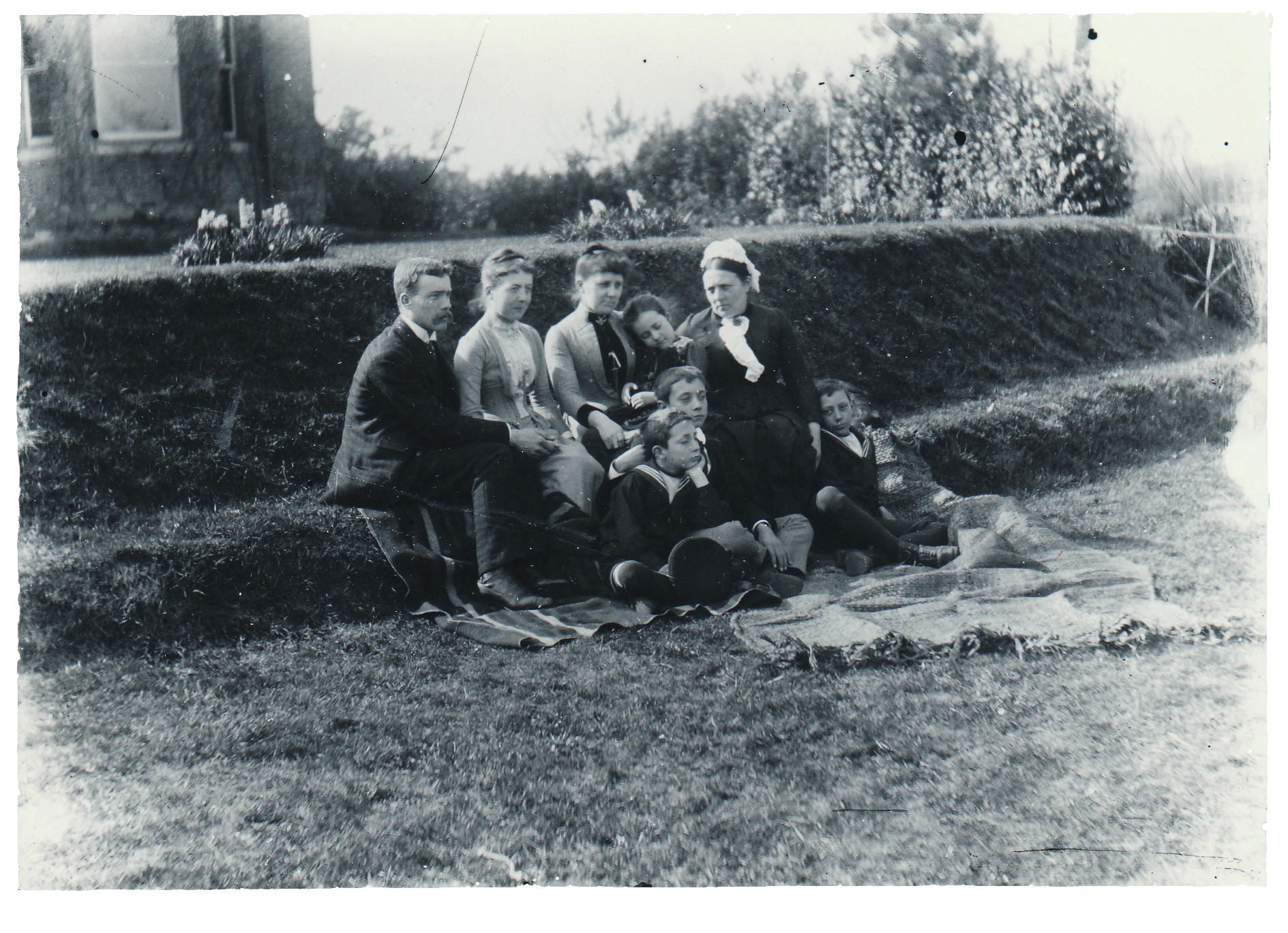 Black and white photograph of a man, two women, a young girl, three boys and a nanny, all wearing Victorian clothes and sitting in a garden