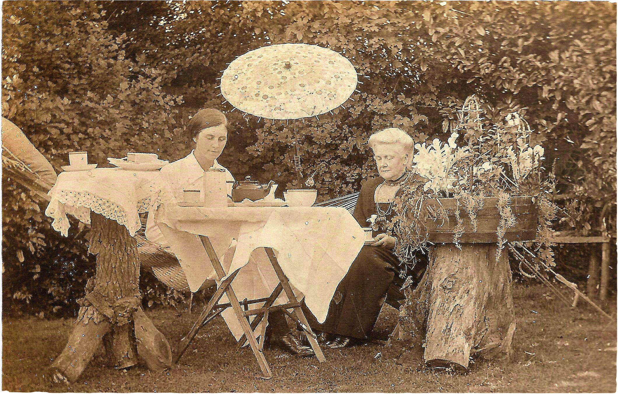 Sepia photograph of two women in Edwardian clothing taking tea in the garden