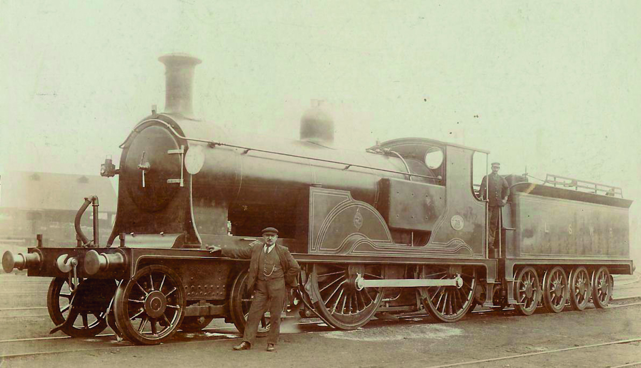 Sepia photograph of a man in old-fashioned clothing standing in front of a steam train
