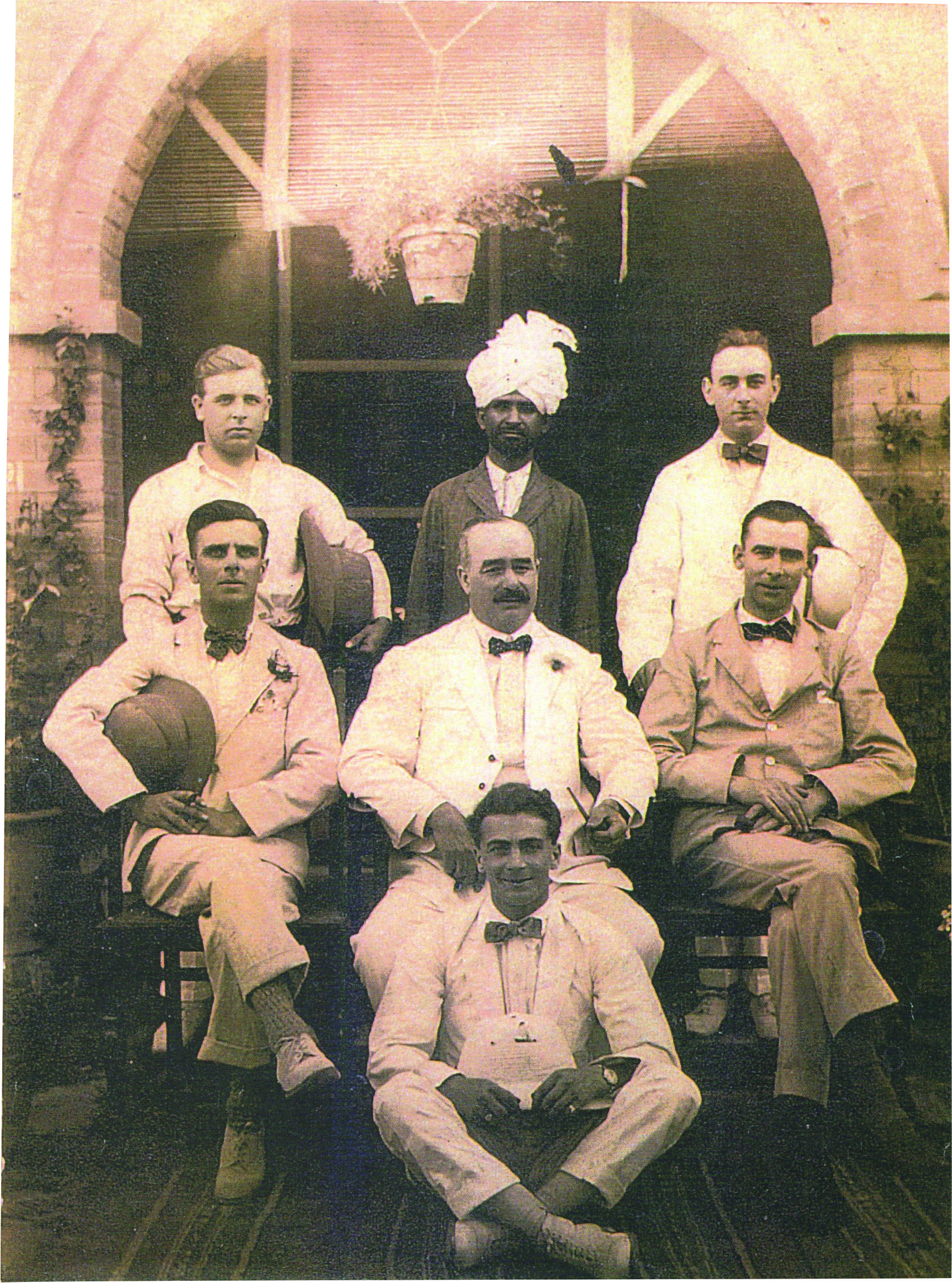 Black and white photograph of six white men in old-fashioned suits with an Indian man in a turban