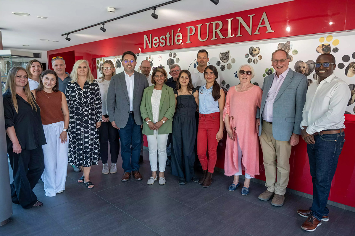 A group of people posing under a sign that says 'Nestle Purina' with photographs of pets